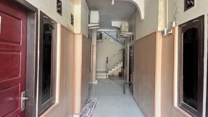 A narrow hallway with a red door on the left, a staircase in the center, and a white door on the right.
