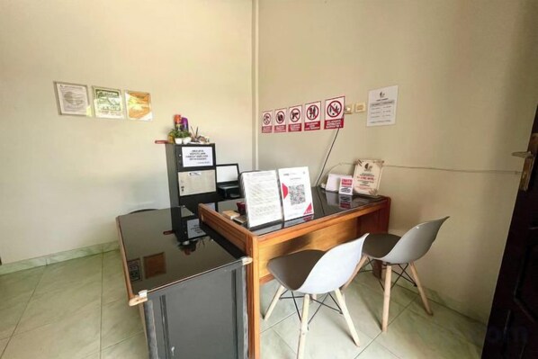 A reception desk with a computer, a small refrigerator, and two chairs. There are signs on the wall and certificates on the wall.