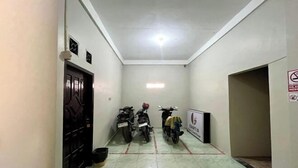 A narrow hallway with two motorcycles parked on the left, a door with a decorative panel, and a sign on the right wall.