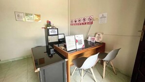 A reception desk with a computer, a small refrigerator, and two chairs. There are signs on the wall and a few framed items on the wall.