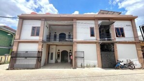 A two-story residential building with a balcony on the upper floor, a gated entrance, and a parked motorcycle.