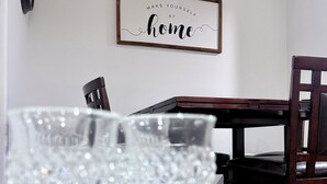 A dining table with crystal glasses, a framed quote on the wall, and a dark wooden chair.