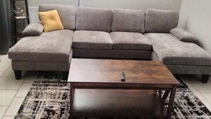 A grey sectional sofa with a yellow accent pillow, a wooden coffee table, and a patterned rug on a tiled floor. - Beautiful remodelded 4/1.5 bathroom home in SOUTH CORPUS CHRISTI, close to beach (Corpus Christi)