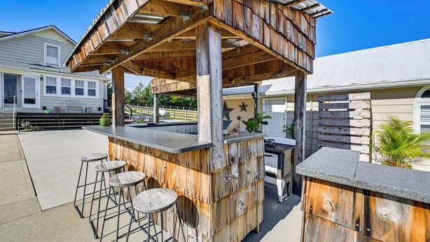 Eine hölzerne Bar im Freien mit Barhocker und Theke, umzäunt und mit einem Haus im Hintergrund.