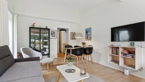 En moderne stue med sofa, sofabord, fjernsyn, bogreol og spiseplads.