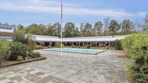 En gårdhave med swimmingpool, flagstang og en bygning med en overdækket terrasse.