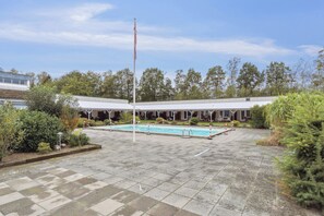 Une cour avec une piscine, un mât pour drapeau et un bâtiment doté d’un patio couvert.