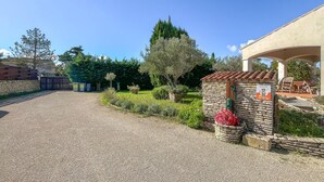 A gravel driveway leading to a stone-built entrance with a small garden area, a pergola with seating, and a clear blue sky. - Amazing home in Aramon with swimming pool (Aramon)