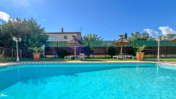 A clear blue swimming pool with lounge chairs and umbrellas, surrounded by a wooden fence and greenery. - Amazing home in Aramon with swimming pool (Aramon)