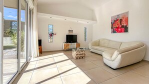 A spacious living room with a sofa, a glass coffee table, a TV, and decorative items. - Cozy home in Serviers-et-Labaume (Serviers-et-Labaume)