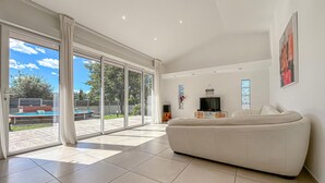 A spacious living room with a large sofa, a television, and a sliding glass door leading to an outdoor area with a pool. - Cozy home in Serviers-et-Labaume (Serviers-et-Labaume)
