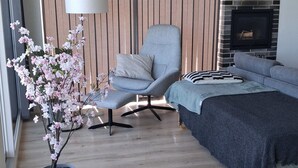 Een moderne woonkamer met een bank, een fauteuil, een salontafel, een potplant en een open haard.