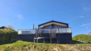 Une maison moderne avec un toit en pente, un espace extérieur couvert et une colline verdoyante.