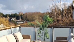 Een houten terras met rieten meubels, waaronder een bank en een tafel met potten.