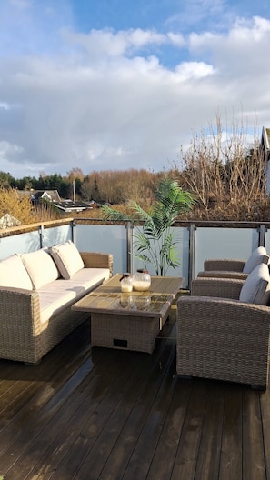 Eine Holzterrasse mit Korbmöbeln, darunter eine Couch und ein Tisch mit Gläsern.