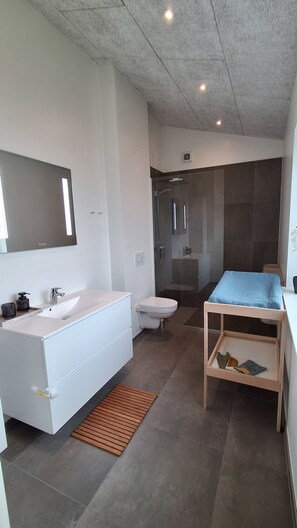 Une salle de bain moderne avec un meuble-lavabo blanc, une cabine de douche en verre et un banc en bois agrémenté d’un coussin.