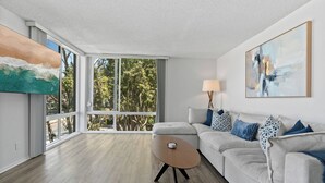 A modern living room with a large window, a grey sofa with patterned cushions, and a wooden coffee table.