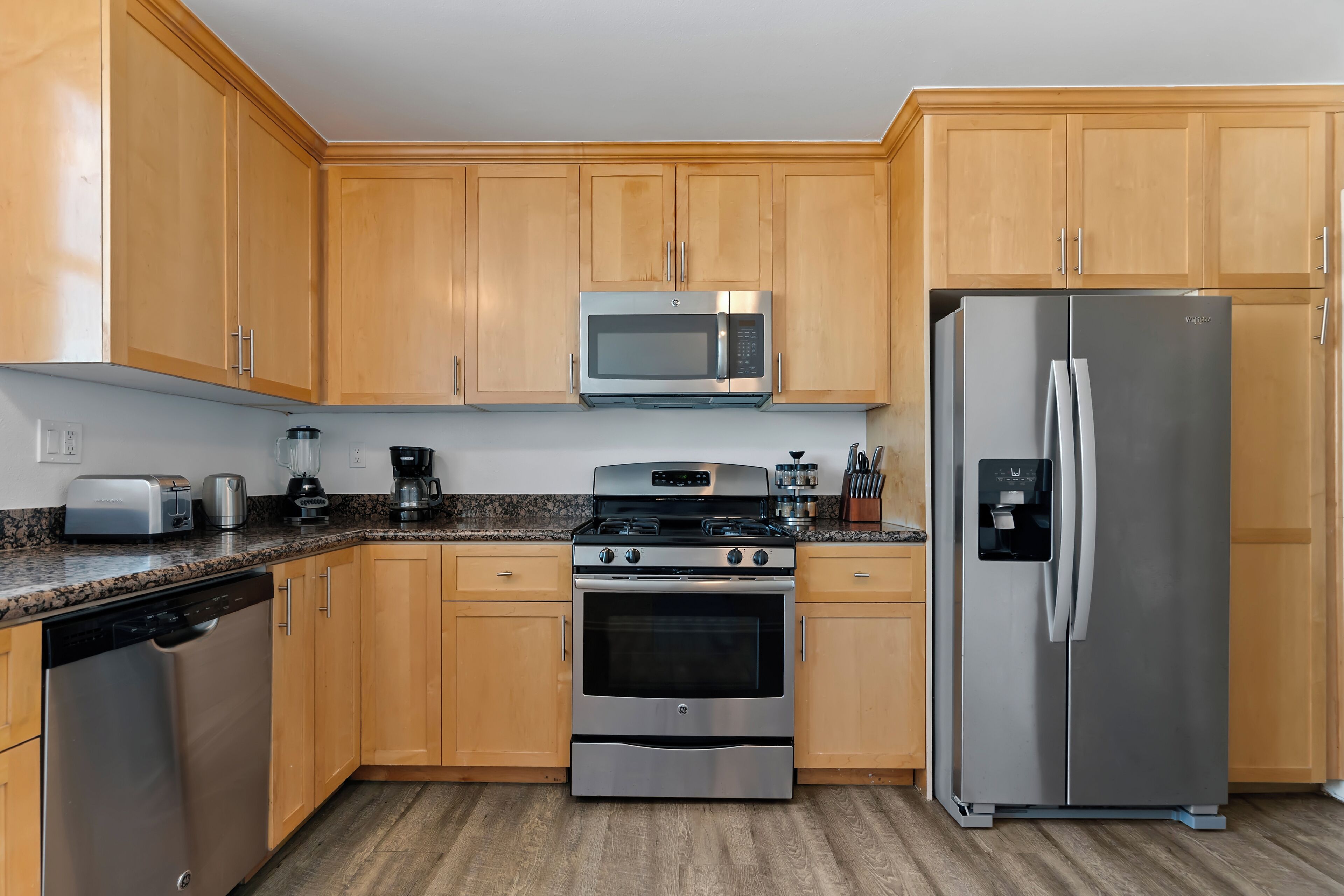 A kitchen with wooden cabinets, stainless steel appliances including a microwave, oven, and refrigerator, a dishwasher, and granite countertops.