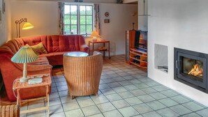 En hyggelig stue med en rød sofa, en fletstol, et lille bord med en lampe, et TV-møbel og en pejs.