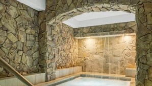 Ein Wellnessbereich mit Steinwand, Whirlpool und Holzbank.