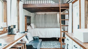 A compact room with a bunk bed, a wooden desk with stools, a small kitchenette, and a ceiling fan. - Charming Tiny Home in Pace Near Downtown and Pensacola Beach, 2 min from Walmart (Pace)