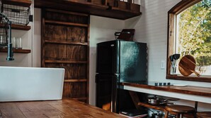 A kitchen with wooden cabinets, a black refrigerator, and a window with a view of trees. - Charming Tiny Home in Pace Near Downtown and Pensacola Beach, 2 min from Walmart (Pace)