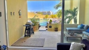 A balcony with a view of a swimming pool, outdoor furniture, and potted plants.