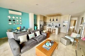 A modern living room with a grey sofa, a wooden coffee table, and a kitchen in the background.