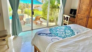 A bedroom with a large bed, a view of a pool and outdoor seating area through a sliding glass door.