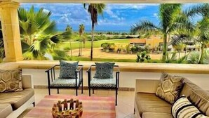 A balcony with two chairs and a sofa, overlooking a tropical landscape with palm trees and a golf course.
