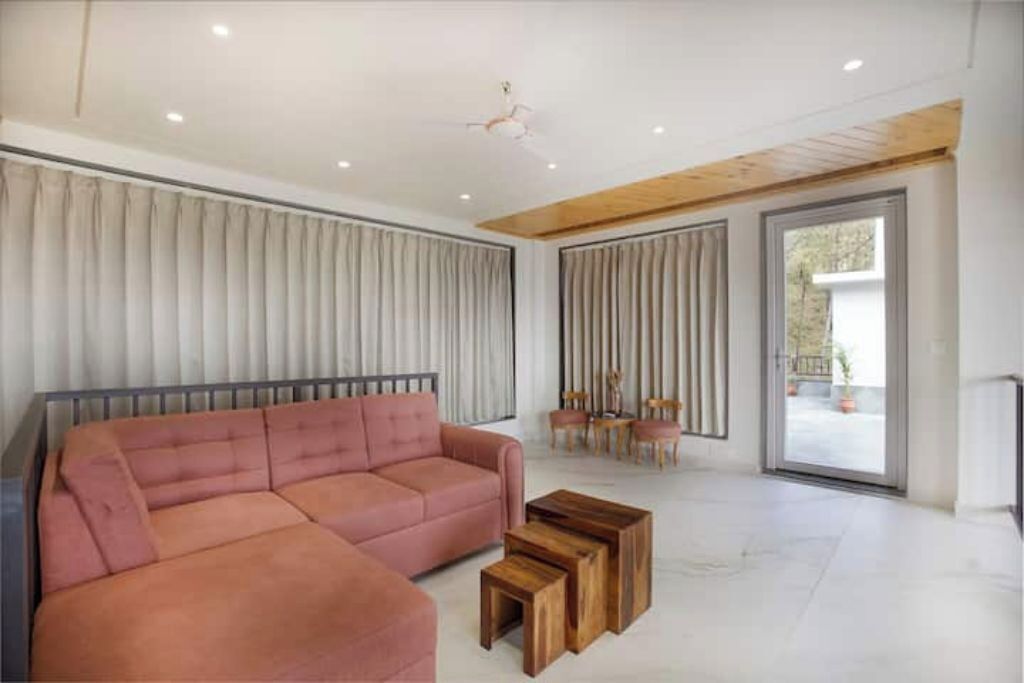 Una sala de estar moderna con un sofá seccional, mesas de centro de madera y un amplio ventanal corredero que da a un área exterior.