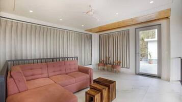 Una sala de estar moderna con un sofá seccional, mesas de centro de madera y un amplio ventanal corredero que da a un área exterior.