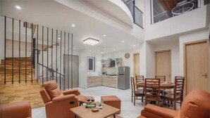 Un vaste espace de vie agrémenté de canapés orange, d’un escalier en bois, d’une cuisine en arrière-plan et d’un coin repas avec une table et des chaises.