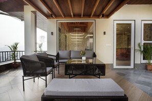 A modern outdoor seating area with a glass table, black wicker furniture, and a view of the sea. - Scarlett Peaks | Luxe 4BHK w/Theatre & Game Lounge (Himachal Pradesh)