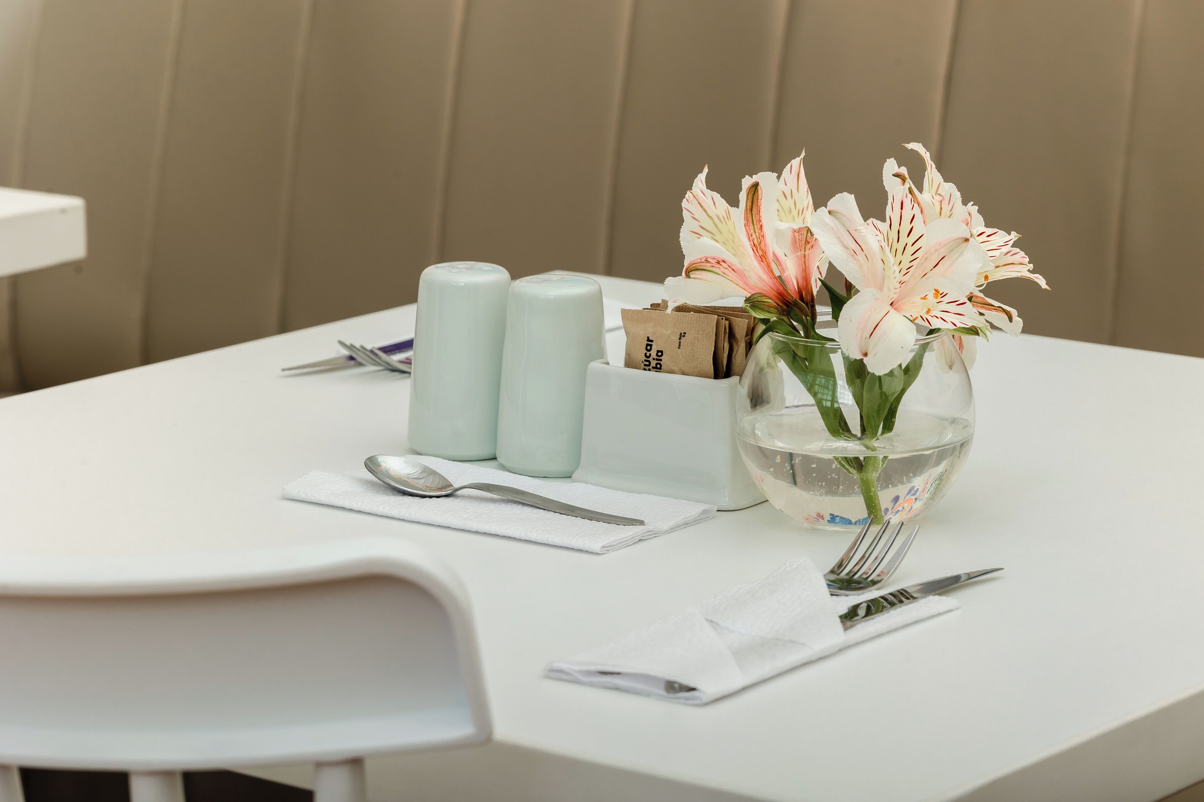 A neatly arranged dining table with a vase of flowers, salt and pepper shakers, a box of tissues, and cutlery.