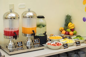 Un bar de zumos con dos dispensadores, una exposición de frutas y cuencos etiquetados con fresas y piña.