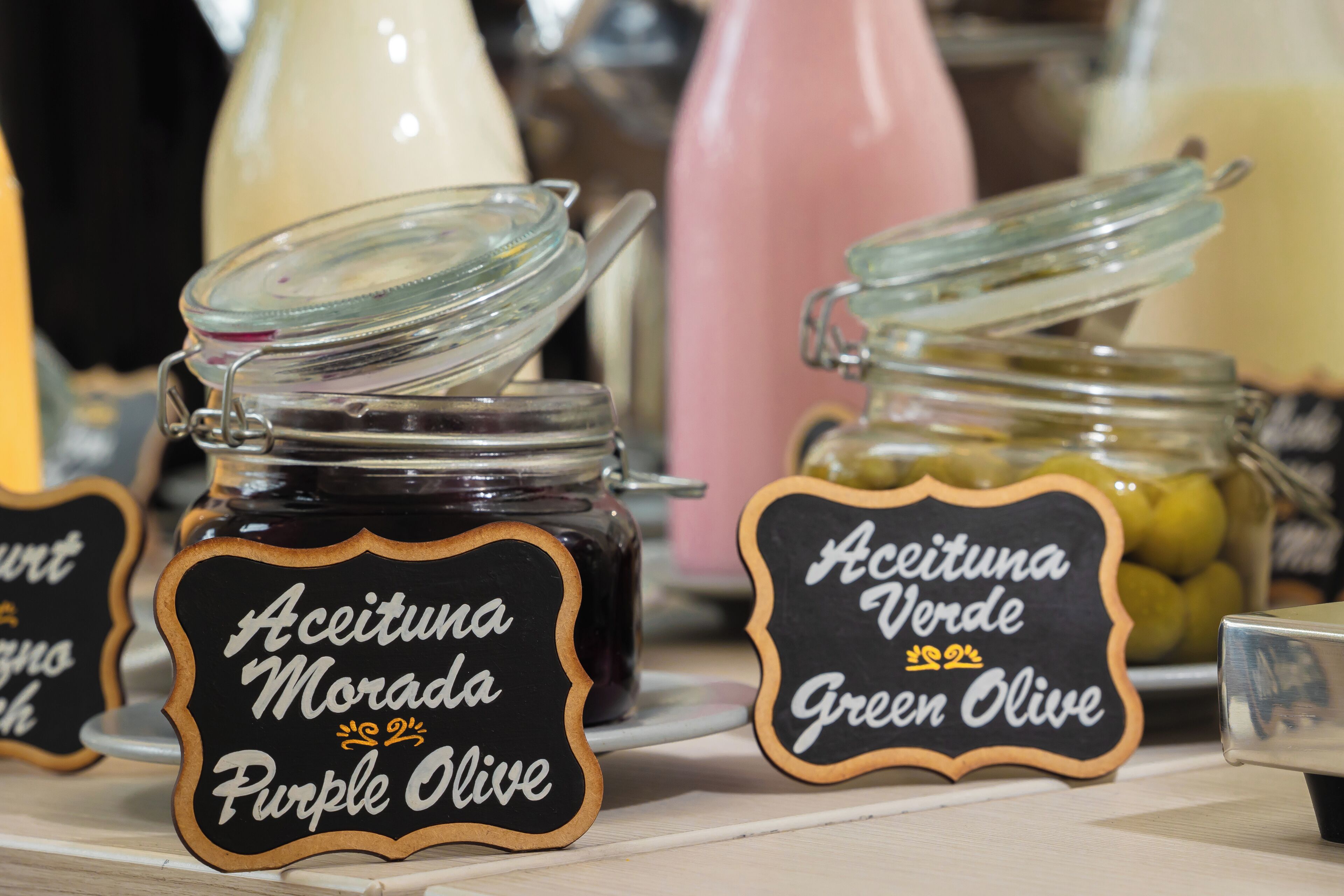 Three glass jars of olive oil with labels indicating different types: purple, green, and green olive.