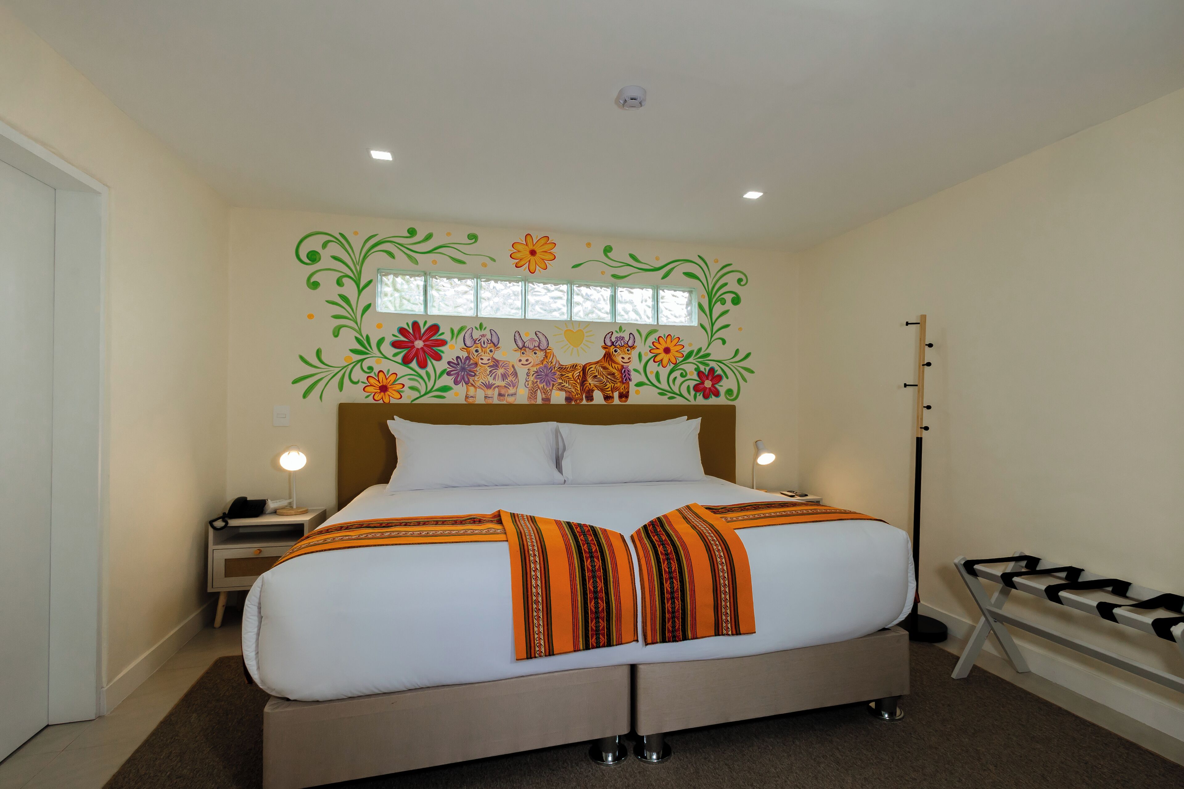 A hotel room with a large bed, a nightstand, a lamp, and a window with decorative wall art.