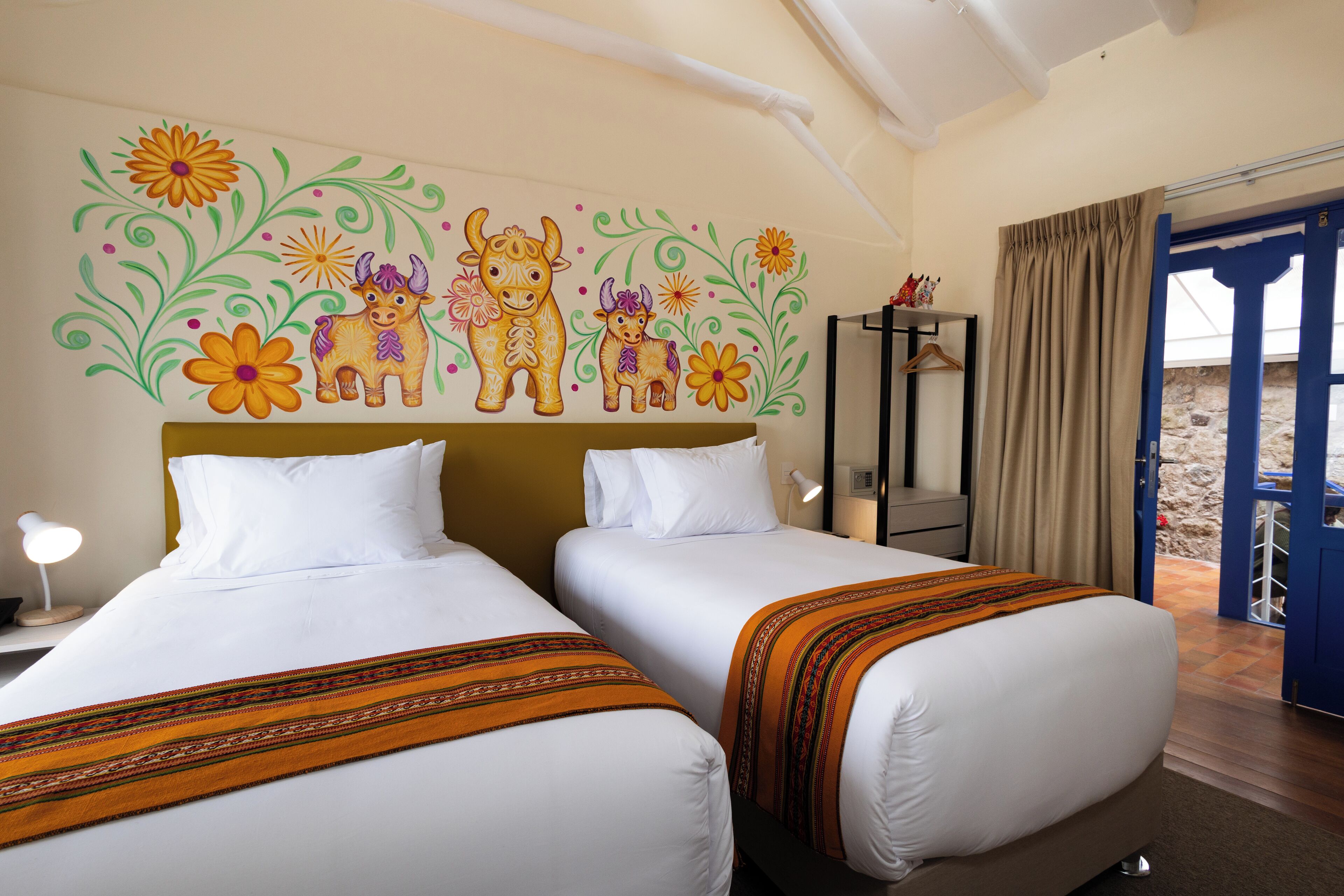 A hotel room with two beds, a decorative wall mural, a nightstand, a lamp, and a view of the outside.