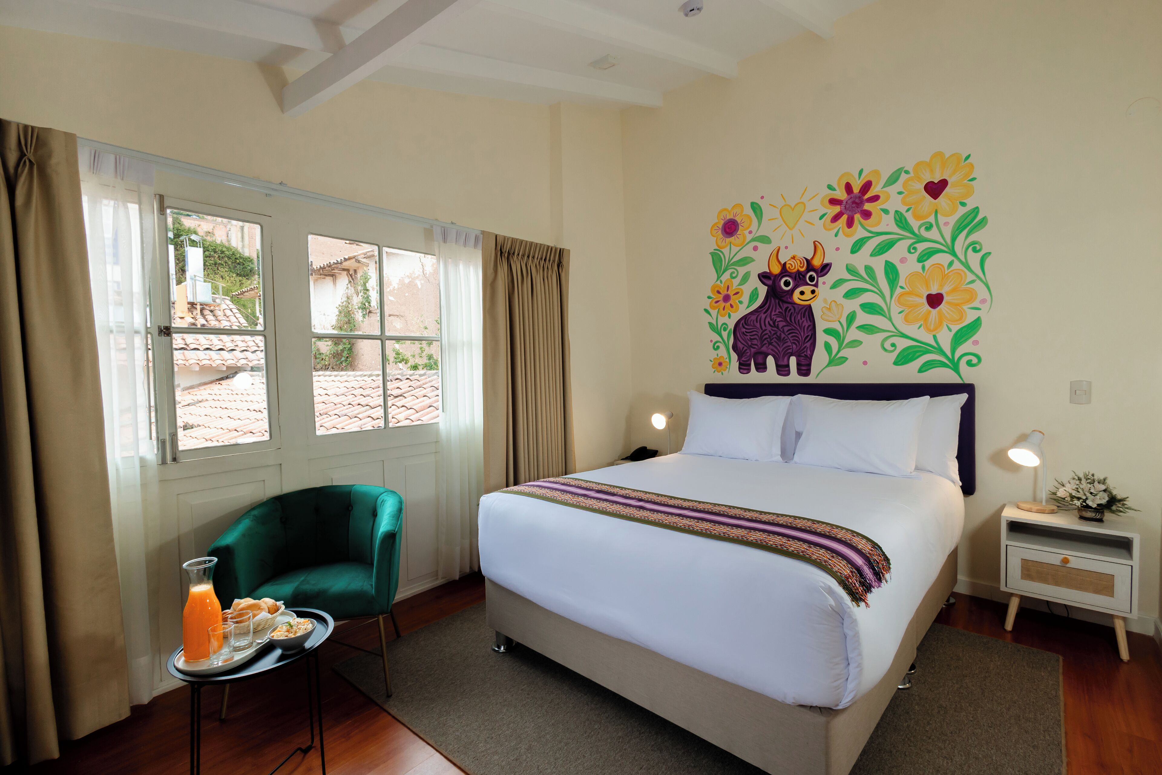 A hotel room with a bed, a green armchair, a small table with breakfast, and a decorative wall mural.