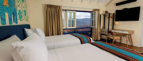 A hotel room with a large bed, a desk, a chair, a TV, and a window with a view of mountains.