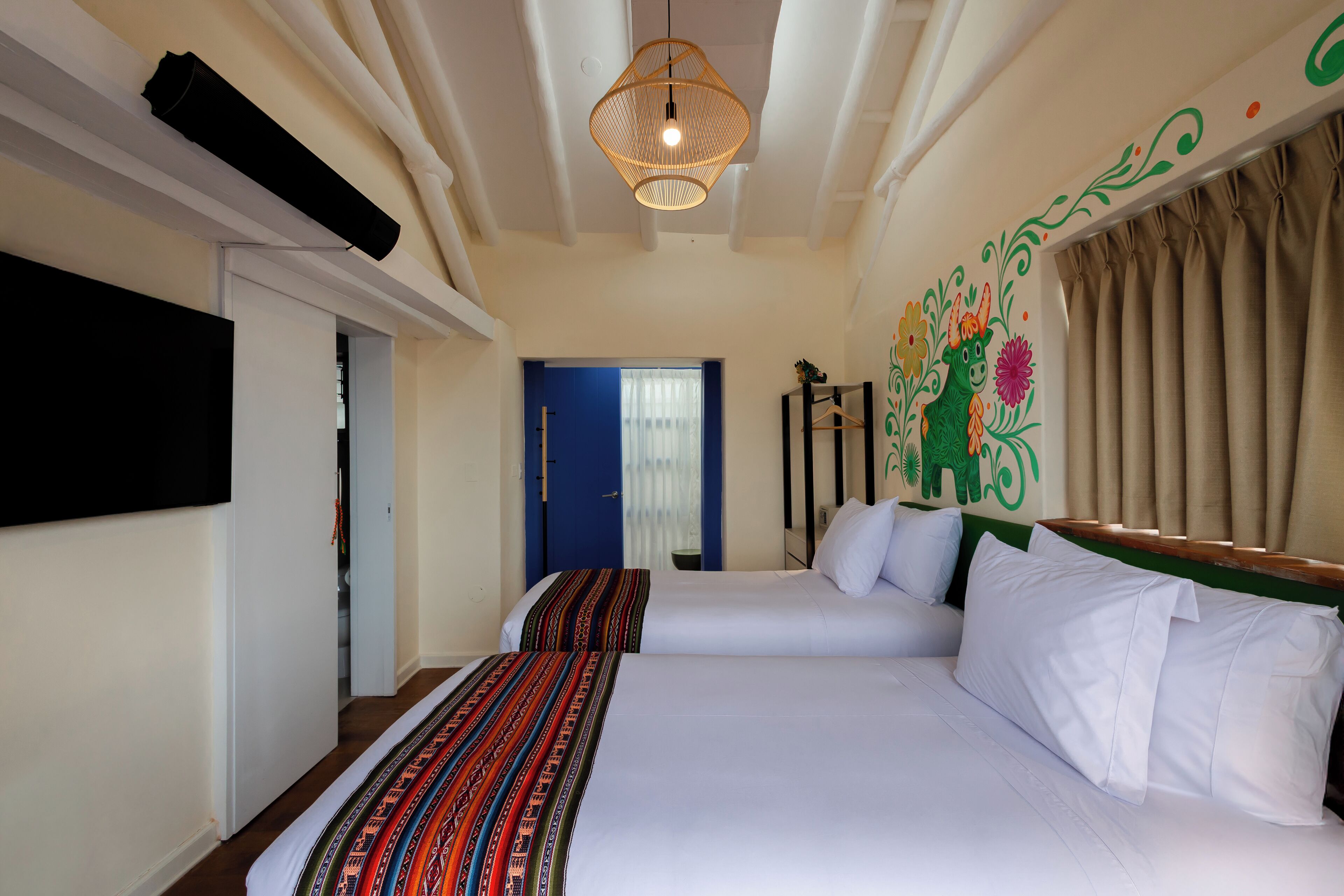 A hotel room with two beds, a television, a decorative wall mural, and a window with curtains.