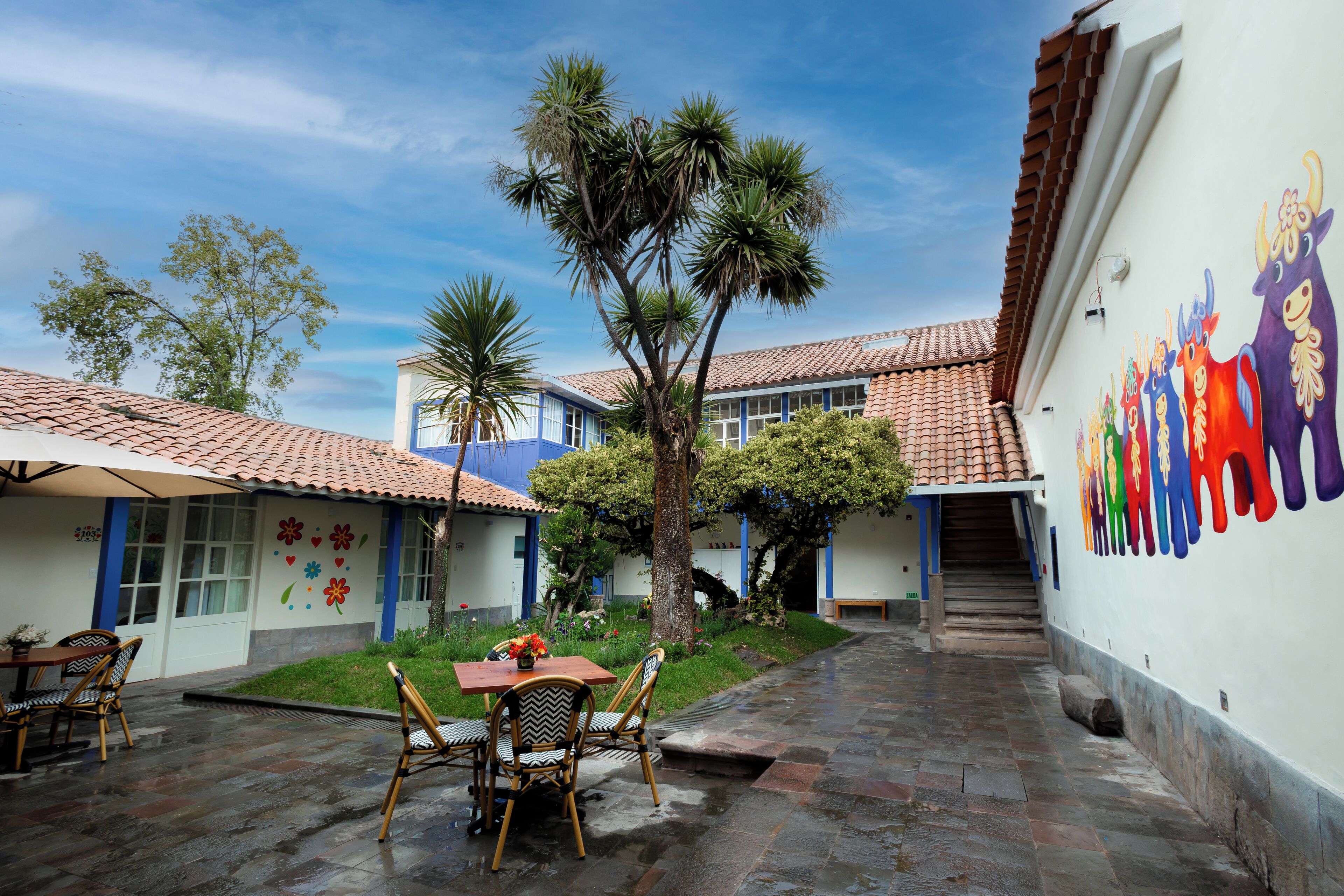 A courtyard with a tiled floor, a wooden table with chairs, and a mural on the wall.