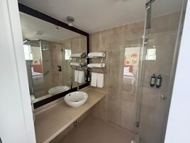 Un baño moderno con un espejo grande, un lavamanos blanco y una cabina de ducha de vidrio.