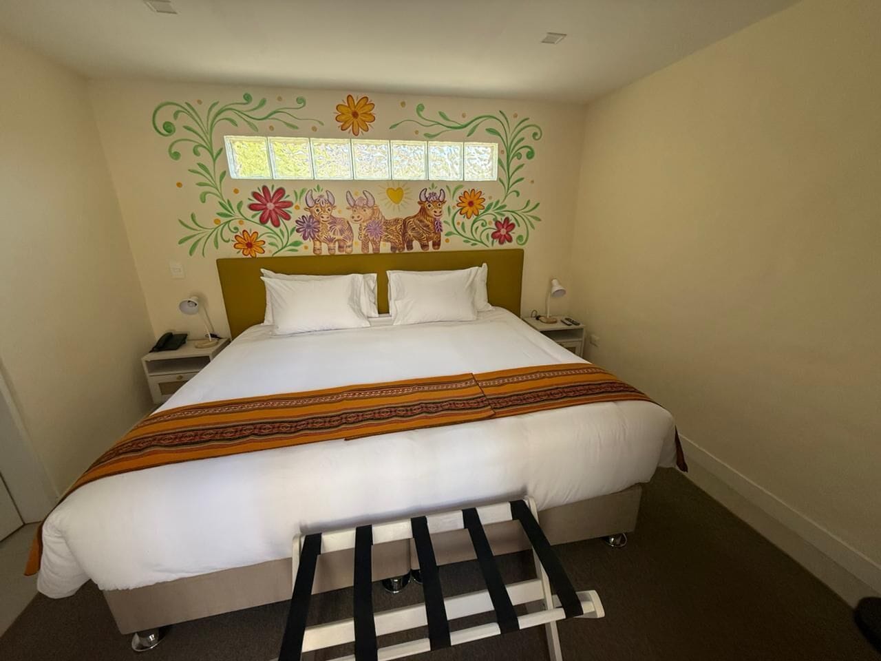 Un lit bien fait, recouvert d’une couvre-lit à motifs, avec une tête de lit ornée de motifs floraux et une petite fenêtre située au-dessus du lit.