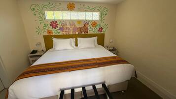 Un lit bien fait, recouvert d’une couvre-lit à motifs, avec une tête de lit ornée de motifs floraux et une petite fenêtre située au-dessus du lit.