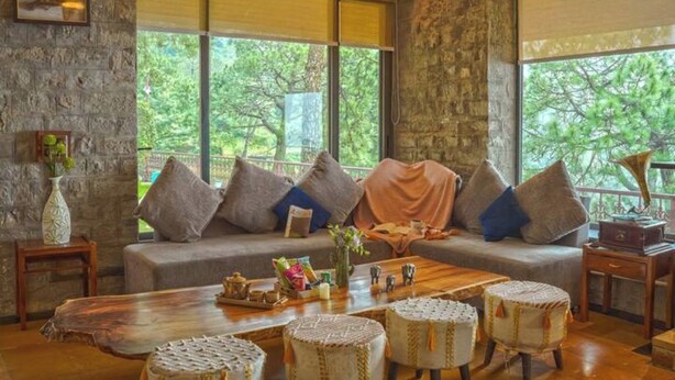 A cozy living room with a stone wall, a sofa with cushions, a wooden coffee table, and wicker ottomans.