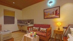 Een gezellige woonkamer met een houten plafond, een bank met kleurrijke kussens, een klein tafeltje met lekkernijen, een lamp en een schilderij aan de muur.
