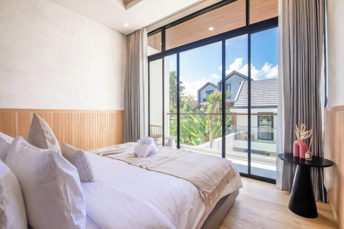 Une chambre d’hôtel avec un grand lit, une vue sur l’extérieur et une petite table sur laquelle est posé un vase.