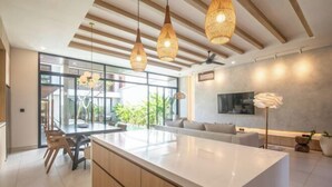 A modern kitchen with a central island, wooden ceiling beams, and hanging wicker pendant lights. - X Samata (Bali)